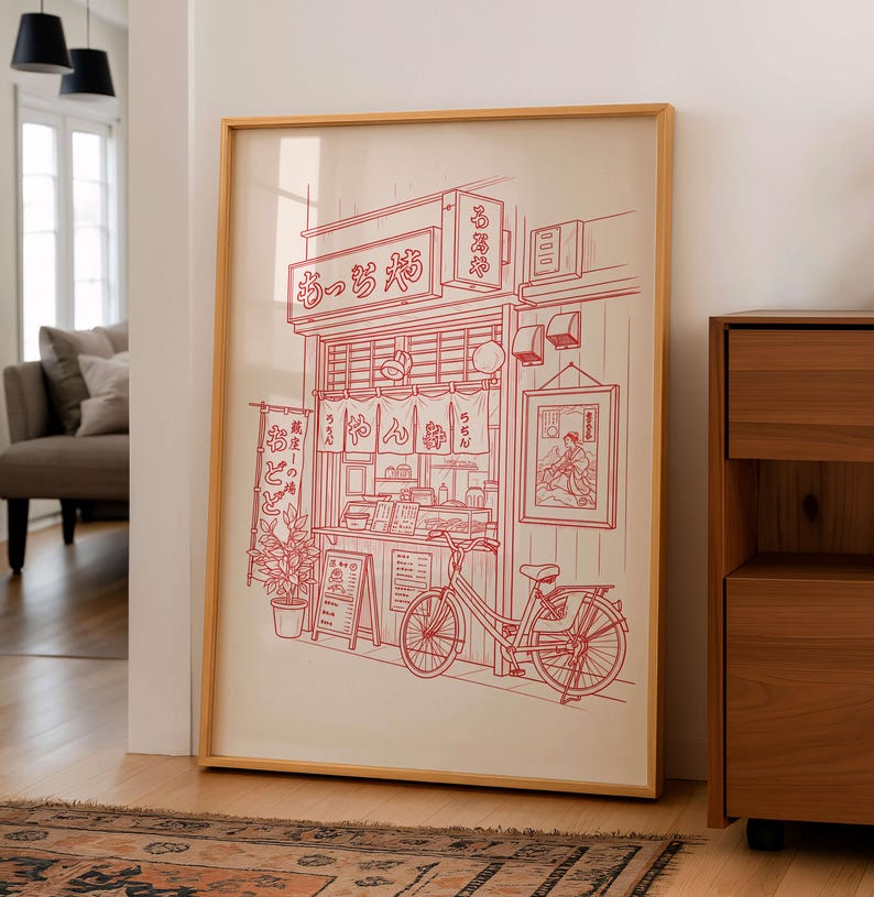 May include: A framed print featuring a red line drawing of a Japanese ramen shop with a bicycle parked in front. The shop has a sign in Japanese and a small menu board. The artwork is in a light wood frame.