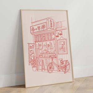 May include: Red line art print of a Japanese restaurant with a bicycle parked outside. The print features a detailed illustration of the shop's facade, signage, and interior details. A potted plant and a menu board are also visible.