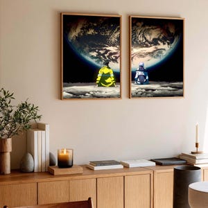 May include: Two framed art prints depict figures seated on a lunar surface, gazing at Earth. One figure wears yellow, the other blue. The artwork features a detailed depiction of the Earth against a dark, starry background.