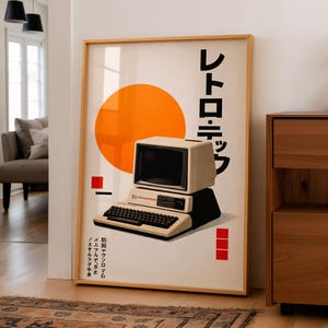 May include: A framed poster featuring a retro computer design with Japanese text. The artwork includes a large orange circle, a beige computer, and red rectangular accents. The poster is displayed in a well-lit room with wooden furniture and a patterned rug.