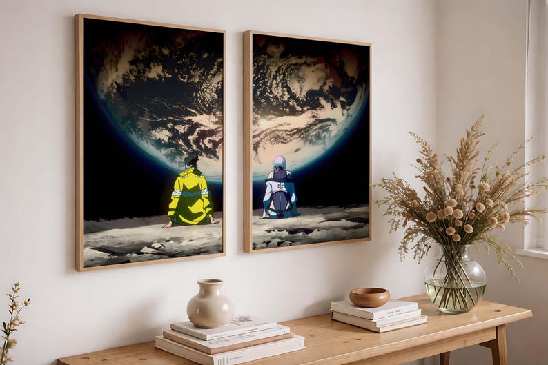 May include: Two framed art prints depict figures seated on a moon-like surface, gazing at Earth. The artwork features a dark space background with a vibrant planet. The figures are in yellow and blue attire. The frames are a light wood color.