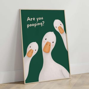 May include: A rectangular wall art print featuring three white geese with orange beaks against a dark green background. The text "Are you pooping?" is printed in white in the upper left corner. The geese have simple black eyes and pink cheeks.