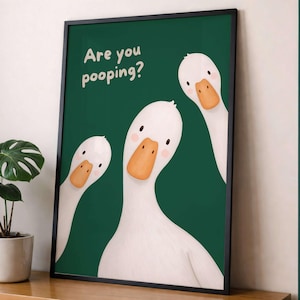 May include: A framed wall art print featuring three white geese with orange beaks against a dark green background. The text "Are you pooping?" is printed in white in the upper left corner. The geese have simple black eyes and pink cheeks.