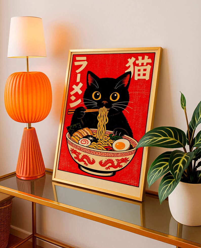 Puede incluir: Un cuadro enmarcado con un gato negro comiendo ramen. La obra, enmarcada en dorado, se encuentra sobre un fondo rojo con caracteres japoneses. Est&aacute; colocado sobre una mesa con tapa de cristal, junto a una l&aacute;mpara naranja y una planta en maceta.