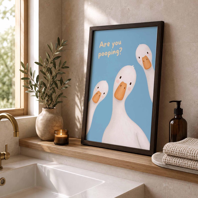 May include: A framed wall art print featuring three white geese with orange beaks against a light blue background. The text "Are you pooping?" is printed in the upper left corner in a light yellow font. The frame is dark brown and rectangular.