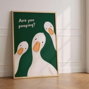 May include: A framed wall art print featuring three white geese with orange beaks against a dark green background. The text "Are you pooping?" is printed in white in the upper left corner. The geese have simple black eyes and pink cheeks.