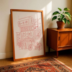 May include: A framed print featuring a red line drawing of a Japanese ramen shop with a bicycle parked outside. The artwork includes Japanese text and details of the shop's facade, displayed in a wooden frame.