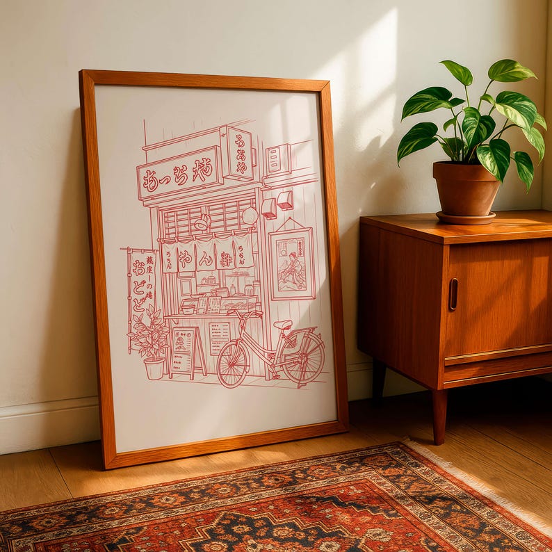 May include: A framed print featuring a red line drawing of a Japanese ramen shop with a bicycle parked outside. The artwork includes Japanese text and details of the shop's facade, displayed in a wooden frame.