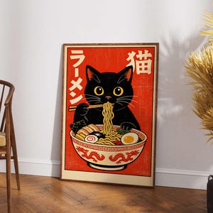 Puede incluir: Un p&oacute;ster enmarcado con un gato negro comiendo ramen. El p&oacute;ster tiene un fondo rojo con texto japon&eacute;s y un cuenco decorativo con un dise&ntilde;o de drag&oacute;n. El gato tiene ojos amarillos y sostiene fideos con palillos.