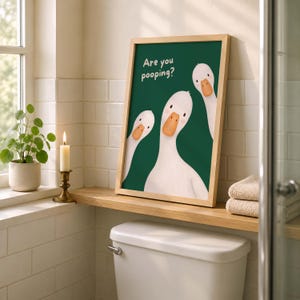 May include: A framed wall art print featuring three white geese with orange beaks against a dark green background. The text "Are you pooping?" is printed in white in the upper left corner. The illustration has a clean, simple aesthetic.