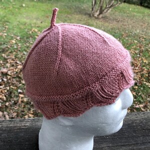 May include: A pink knitted hat with a pointed top and a scalloped brim.