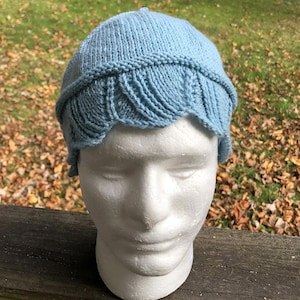 May include: A light blue knitted hat with a scalloped edge. The hat is on a white styrofoam head.