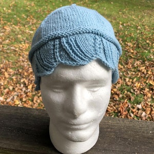 May include: A light blue knitted hat with a scalloped edge. The hat is on a white styrofoam head.