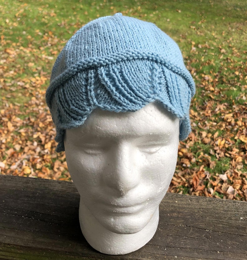 May include: A light blue knitted hat with a scalloped edge. The hat is on a white styrofoam head.