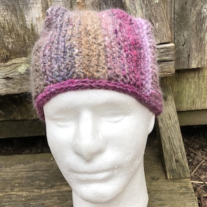 May include: A crocheted hat with a pink, brown and purple striped pattern. The hat has a pink crocheted brim.