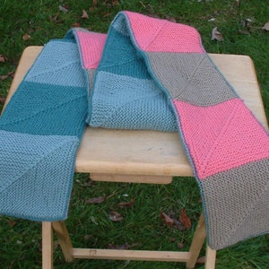 May include: A knitted scarf with a geometric pattern in shades of teal, blue, pink, and brown.