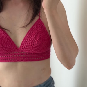 Pode incluir: Top de crochê magenta com decote em forma de triângulo e alças finas. O top apresenta um design detalhado de tecido aberto na borda inferior. A peça de roupa feita à mão é uma peça elegante.