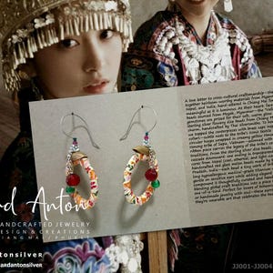 May include: Handmade silver earrings with colorful fabric hoops, red and green beads, and dangling chains. The earrings are part of the Richard Anton Silver collection, with the brand's logo and contact information visible.