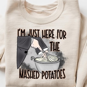Może przedstawiać: Beżowa bluza z napisem "I'm just here for the mashed potatoes" i kreskówkową ilustracją ręki mieszającej miskę ziemniaków puree.