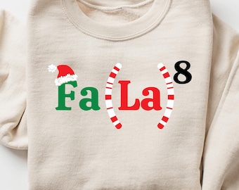 May include: A beige sweatshirt with a Christmas-themed design featuring the text "Fa La 8" with candy cane graphics and a Santa hat.