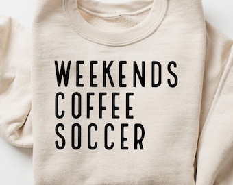 Puede incluir: Sudadera beige con las palabras "WEEKENDS COFFEE SOCCER" impresas en negro. Las mangas están enrolladas. La sudadera es de estilo casual, perfecta para el uso diario.