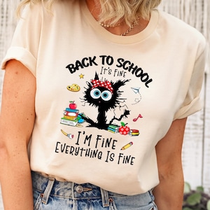 Könnte beinhalten: Ein hellbeiges T-Shirt mit einer schwarzen Katzenillustration und dem Text "Back to School It's Fine I'm Fine Everything Is Fine".