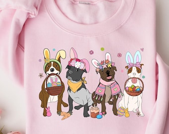 May include: Pink sweatshirt with a graphic of four dogs wearing bunny ears and holding Easter baskets. The dogs are wearing floral headbands and are surrounded by flowers and Easter eggs.