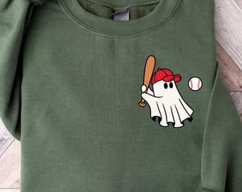 May include: A green sweatshirt with a white ghost wearing a red baseball cap and holding a bat. The ghost is hitting a white baseball with red stitching.