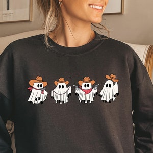 May include: Black sweatshirt featuring a design of five ghosts wearing cowboy hats and holding guns. The ghosts are white and the hats are brown.