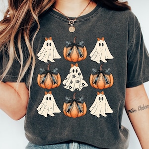 Puede incluir: Una camiseta gris oscuro con un dise&ntilde;o de tem&aacute;tica de Halloween con fantasmas blancos y calabazas naranjas con lazos negros. Las calabazas tienen un dise&ntilde;o de encaje blanco.