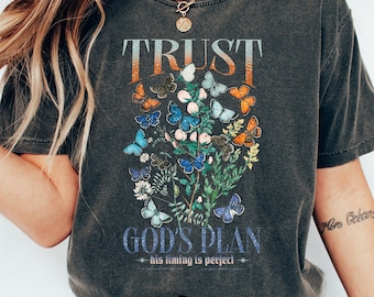 May include: A grey t-shirt with a vintage-style graphic featuring butterflies and the text "TRUST GOD'S PLAN - his timing is perfect".