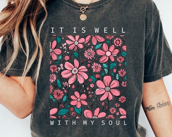 Puede incluir: Una camiseta gris oscuro con un diseño floral y el texto "It is well with my soul".