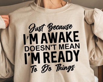 May include: Beige sweatshirt with black text that reads "Just Because I'm Awake Doesn't Mean I'm Ready To Do Things".
