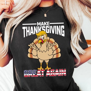 May include: Black t-shirt with a white graphic of a turkey with a blonde hairstyle and the text "MAKE THANKSGIVING GREAT AGAIN" with an American flag design.