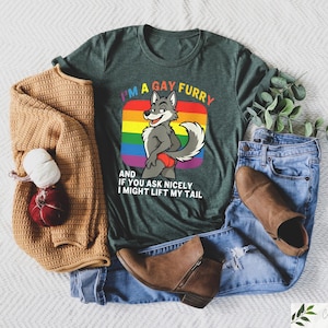 May include: A dark green t-shirt with the text "I'M A GAY FURRY" and a cartoon wolf graphic. The image includes a tan sweater, blue jeans, and brown boots. A red and white decorative item is also present.