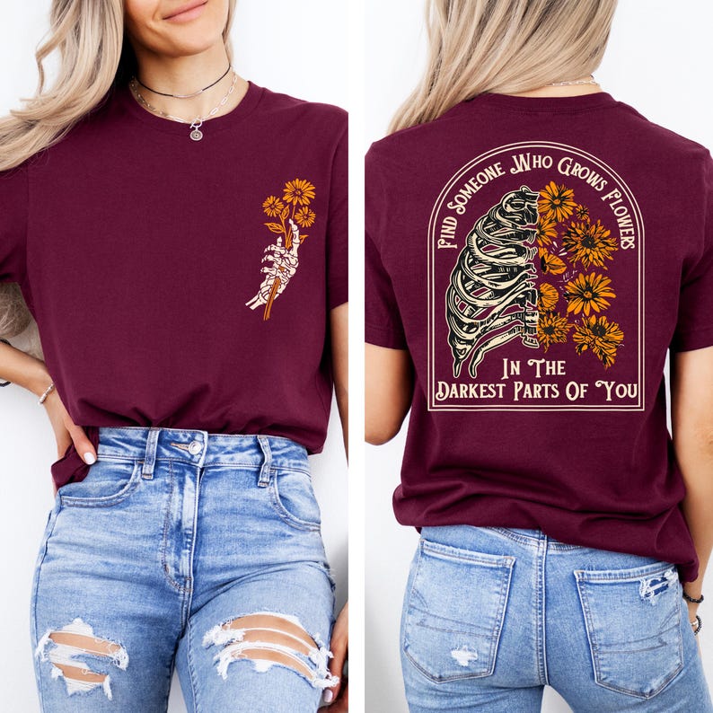 May include: Burgundy t-shirt with a floral and skeleton hand graphic on the front. The back of the shirt features a rib cage design with flowers and the text "Find Someone Who Grows Flowers In The Darkest Parts Of You."