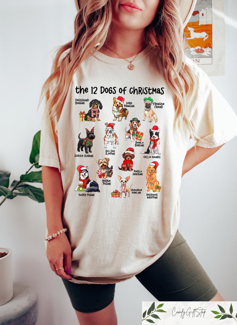 May include: Cream-colored t-shirt featuring the text "the 12 DOGS of CHRISTMAS" above illustrations of various dog breeds, each adorned with festive holiday attire. The shirt includes Dachshunds, Frenchies, Huskies, and more.