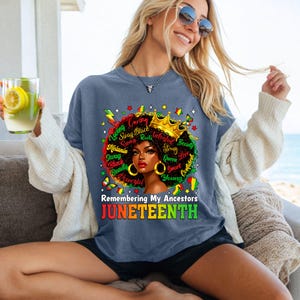 Puede incluir: Una camiseta azul de Juneteenth con un gr&aacute;fico de una mujer negra con una corona dorada y pendientes dorados. La camiseta tiene el texto "Remembering My Ancestors" y "JUNETEENTH" en rojo, verde y amarillo.