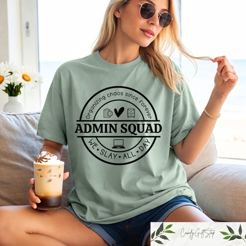 Pu&ograve; includere: Una maglietta verde chiaro con una grafica circolare nera che dice "Organizzare il caos da sempre" e "Admin Squad" con icone di un calendario, un cuore e un archivio. La grafica dice anche "We slay all day".