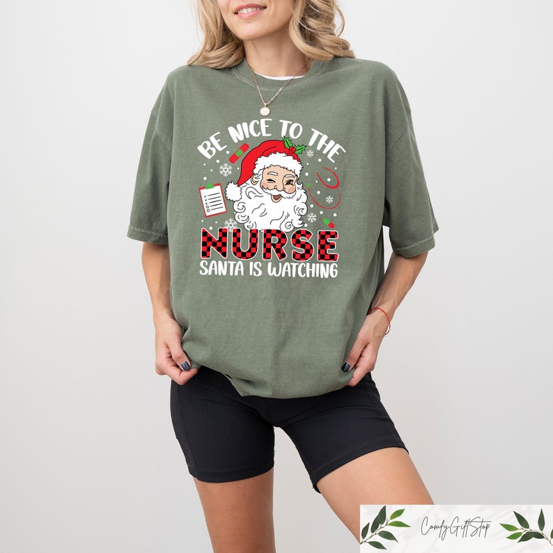 May include: Green t-shirt with a Santa Claus graphic and the text "Be Nice To The Nurse Santa Is Watching".