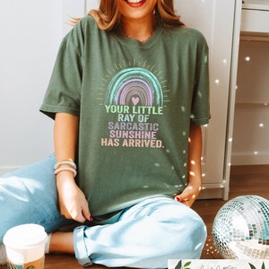 May include: A green t-shirt with a rainbow graphic and the text "Your little ray of sarcastic sunshine has arrived."
