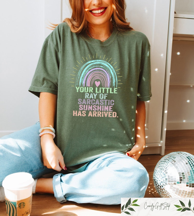 May include: A green t-shirt with a rainbow graphic and the text "Your little ray of sarcastic sunshine has arrived."