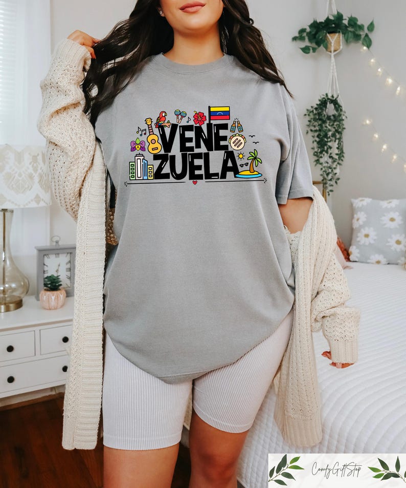 May include: A gray t-shirt with a black graphic design that says "VENEZUELA" with colorful icons representing Venezuelan culture.