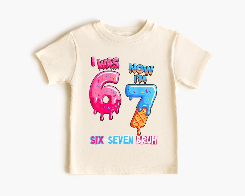 May include: Cream-colored youth t-shirt with a colorful graphic. The graphic reads "I WAS 6 NOW I'M 7 SIX SEVEN BRUH" with the numbers designed as dripping ice cream cones. The number 6 is pink, and the number 7 is blue and orange.
