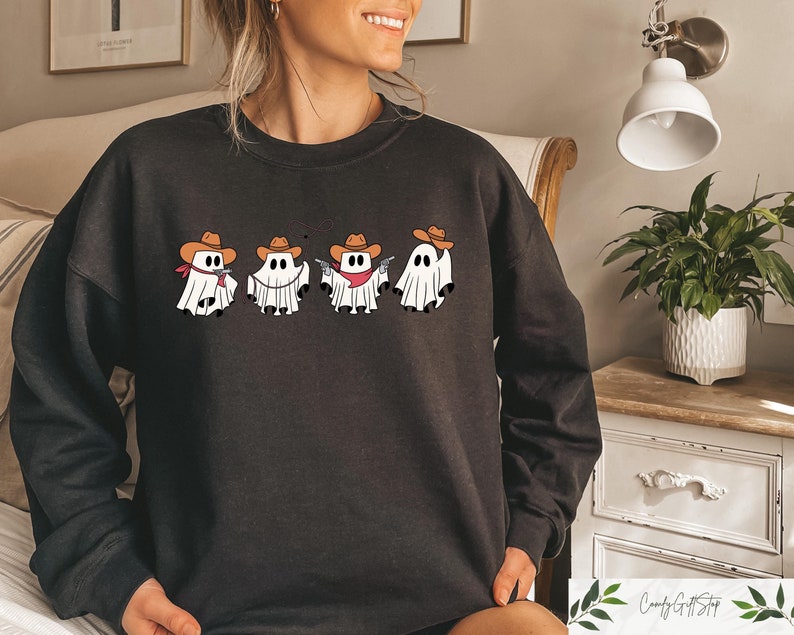 May include: Black sweatshirt featuring a design of five ghosts wearing cowboy hats and holding guns. The ghosts are white and the hats are brown.