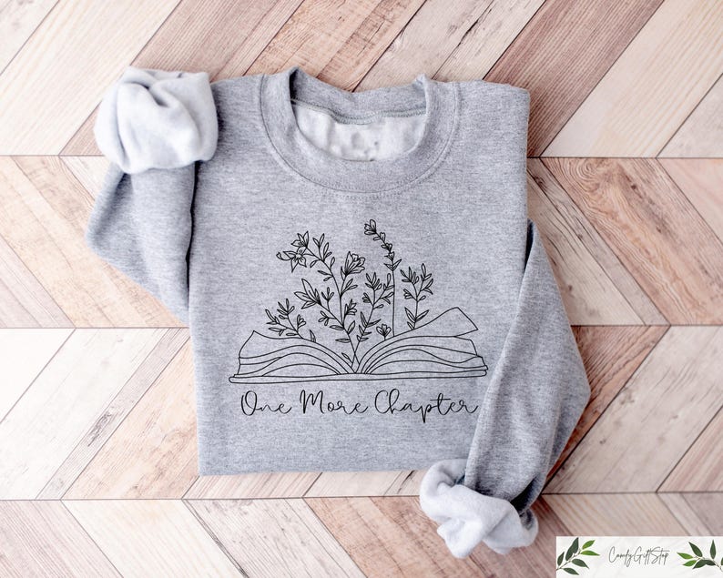 May include: A gray sweatshirt with a black and white illustration of an open book with flowers growing out of it. The text "One More Chapter" is printed below the illustration.