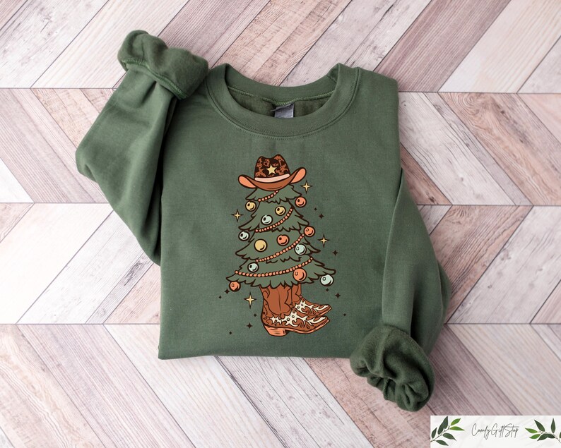 Pu&ograve; includere: Una felpa verde con un disegno di albero di Natale. L'albero indossa un cappello da cowboy e stivali. L'albero &egrave; decorato con ornamenti e luci.