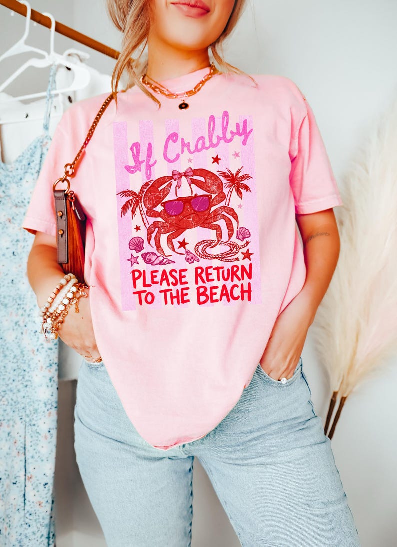 May include: Pink t-shirt with a crab graphic wearing sunglasses and the text "If Crabby Please Return to the Beach." The crab design is red with palm trees and seashells. The shirt is a casual, beach-themed apparel.