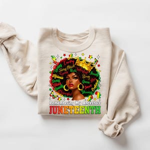 Puede incluir: Una sudadera crema con un gr&aacute;fico de una mujer negra con corona y pendientes dorados, con un afro colorido. El dise&ntilde;o incluye las palabras "Loving, Caring, Swag, Black, Beauty, Powerful, Strong, Queen, Confident, Young" y el texto "Remembering My Ancestors JUNETEENTH."