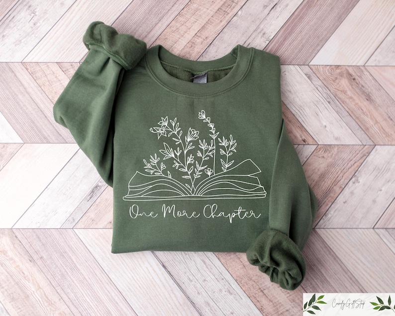 May include: A green sweatshirt with a white design of an open book with flowers growing out of it. The text "One More Chapter" is printed below the book.